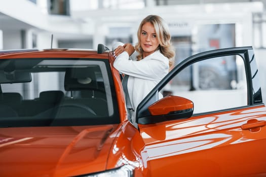 Opening the door. Woman in formal clothes is indoors in the autosalon.