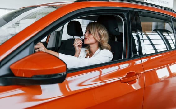 Sitting in the car. Woman in formal clothes is indoors in the autosalon.