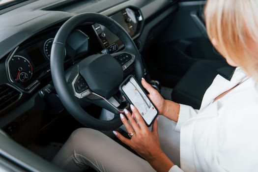 Sitting in the car. Woman in formal clothes is indoors in the autosalon.