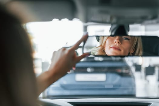 In the car. Woman in formal clothes is indoors in the autosalon.