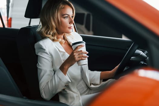 In the car. Woman in formal clothes is indoors in the autosalon.
