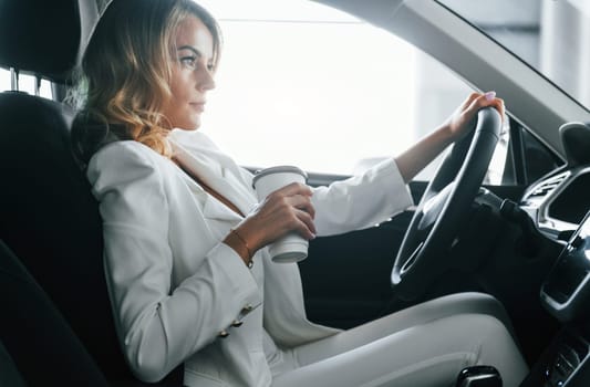 Vehicle interior. Woman in formal clothes is indoors in the autosalon.
