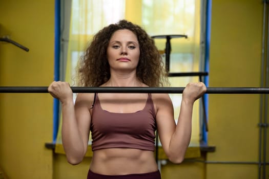 A young girl working out at the gym lifts a barbell to chest height. Using sports equipment at a professionally equipped gym. Taking care of health through physical exercise.