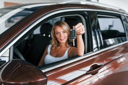 Holding car keys. Woman in formal clothes is indoors in the autosalon.
