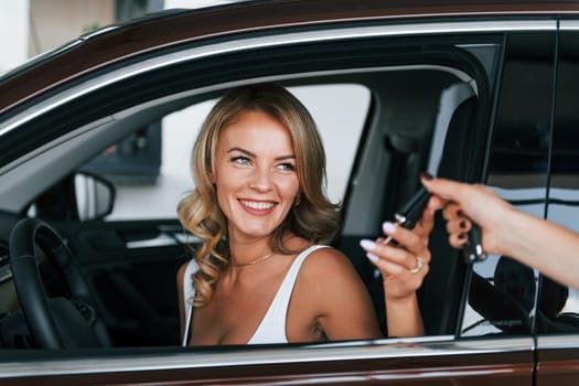 Holding car keys. Woman in formal clothes is indoors in the autosalon.