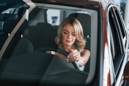 Comfortable car. Woman in formal clothes is indoors in the autosalon.