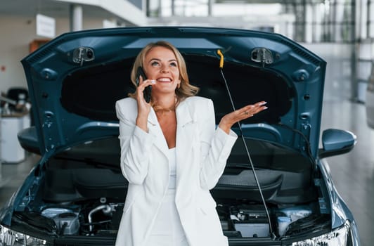 Talking by phone. Woman in formal clothes is indoors in the autosalon.