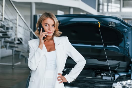 Talking by phone. Woman in formal clothes is indoors in the autosalon.