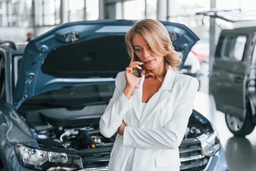 Talking by phone. Woman in formal clothes is indoors in the autosalon.