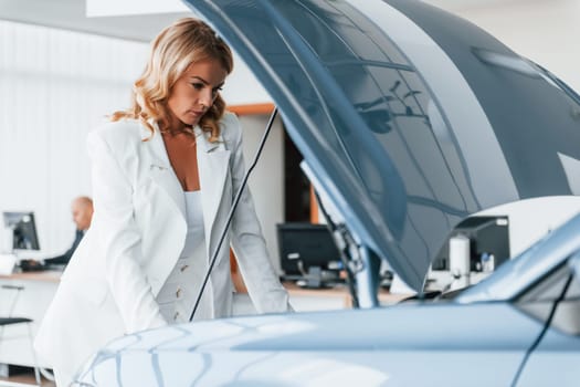 Under the car hood. Woman in formal clothes is indoors in the autosalon.