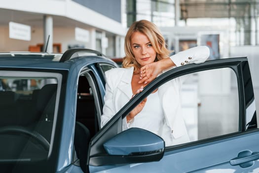 Posing for the camera. Woman in formal clothes is indoors in the autosalon.