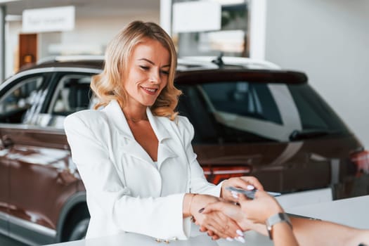 Paying for the product. Woman in formal clothes is indoors in the autosalon.