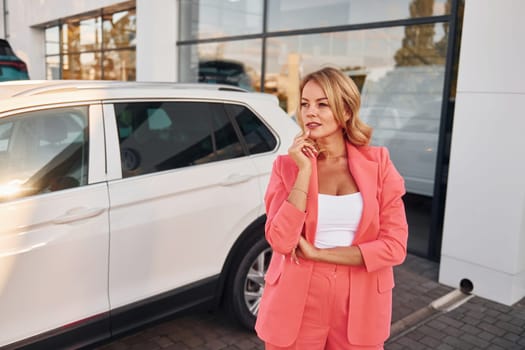 Having conversation by phone. Woman in formal wear standing outdoors with phone in hands and near car.
