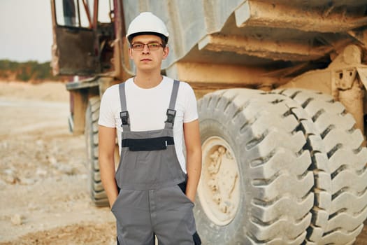 Near loading vehicle. Worker in professional uniform is on the borrow pit at daytime.