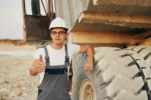 Near loading vehicle. Worker in professional uniform is on the borrow pit at daytime.