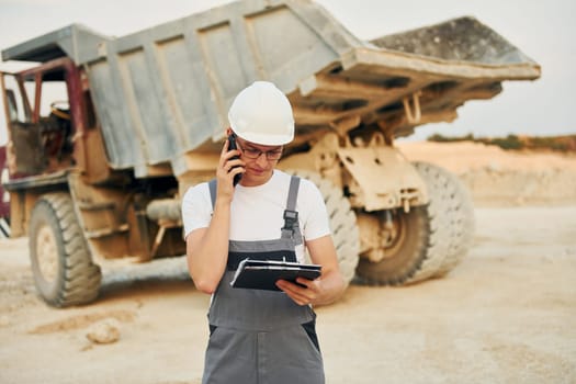 Near loading vehicle. Worker in professional uniform is on the borrow pit at daytime.