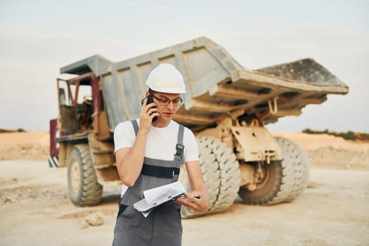 In white hard hat. Worker in professional uniform is on the borrow pit at daytime.