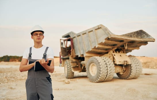 In white hard hat. Worker in professional uniform is on the borrow pit at daytime.