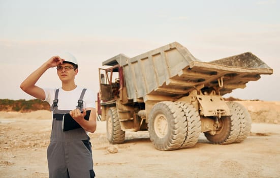In white hard hat. Worker in professional uniform is on the borrow pit at daytime.