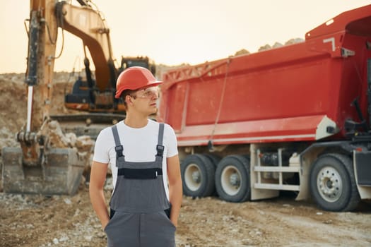 In front of vehicle. Worker in professional uniform is on the borrow pit at daytime.