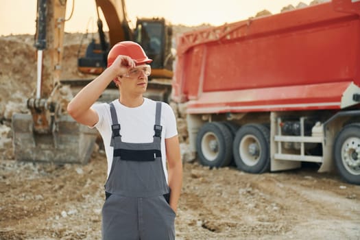 In front of vehicle. Worker in professional uniform is on the borrow pit at daytime.