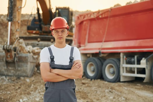 In front of vehicle. Worker in professional uniform is on the borrow pit at daytime.