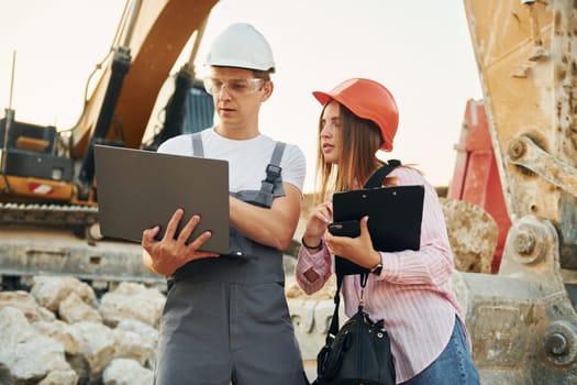 Using laptop. Two workers is on the borrow pit at daytime together.