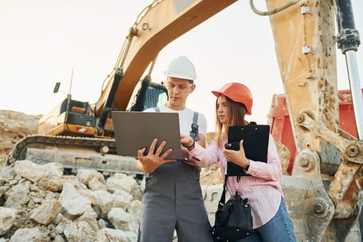 Using laptop. Two workers is on the borrow pit at daytime together.