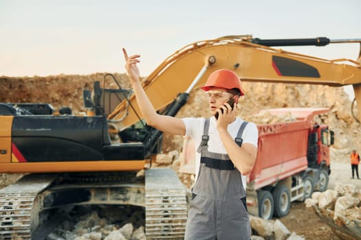 Holding documents in hands. Worker in professional uniform is on the borrow pit at daytime.