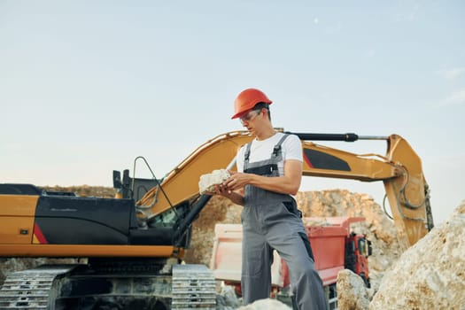 Holding documents in hands. Worker in professional uniform is on the borrow pit at daytime.