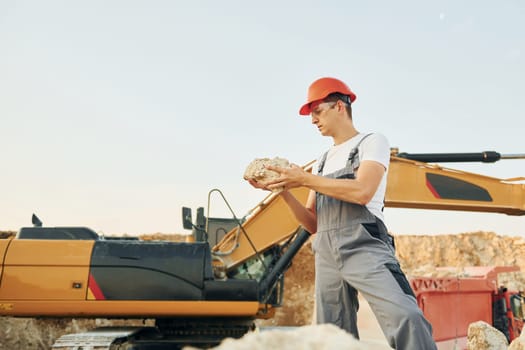 Holding documents in hands. Worker in professional uniform is on the borrow pit at daytime.
