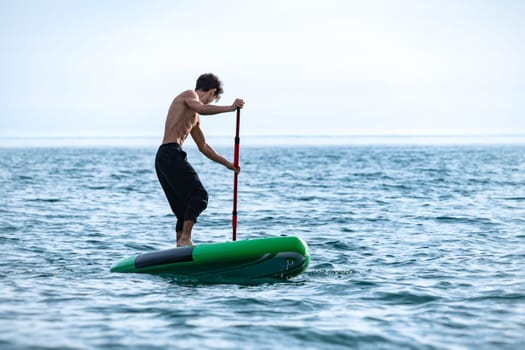 a sporty guy swims on a sup board with a paddle on the sea during the day against a beautiful sky in summer