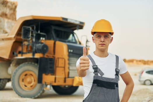 In glasses and hard hat. Worker in professional uniform is on the borrow pit at daytime.