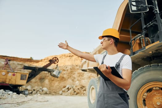 Quality vehicle. Worker in professional uniform is on the borrow pit at daytime.