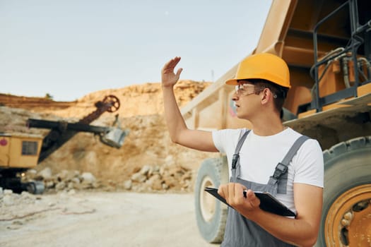 Quality vehicle. Worker in professional uniform is on the borrow pit at daytime.