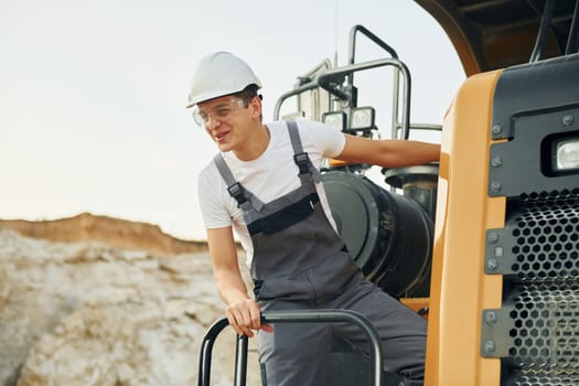 On the vehicle. Worker in professional uniform is on the borrow pit at daytime.