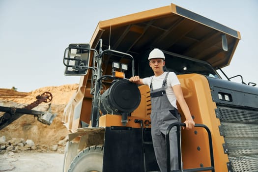On the vehicle. Worker in professional uniform is on the borrow pit at daytime.