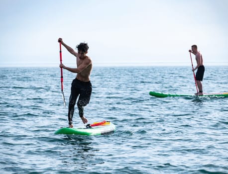 a sporty guy swims on a sup board with a paddle on the sea during the day against a beautiful sky in summer