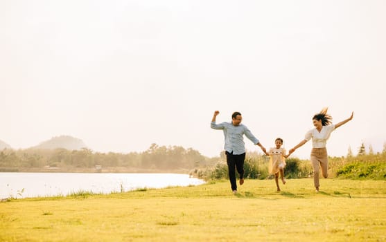 A group of family father, mother and child running and playing in a beautiful nature setting, with green grass and a sunny sky, feeling free and happy, Happy Family Day Concept