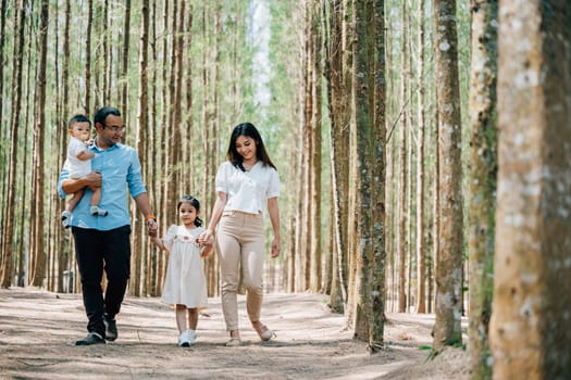 Parents holding their young son's hand and walking through the forest, enjoying the nature and fresh air, Happy family day