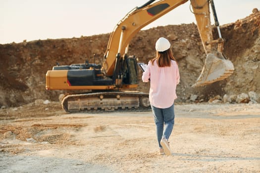 With documents. Young woman with documents in hard hat is standing on the borrow pit.