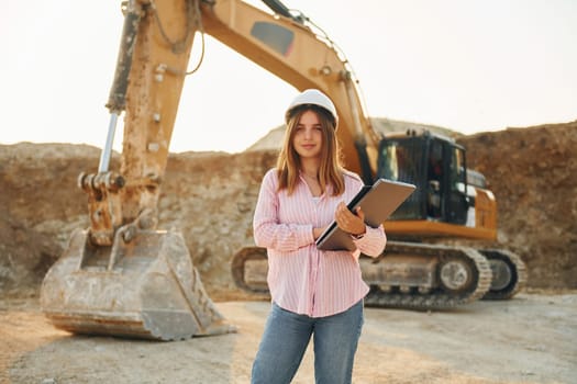 Young woman with documents in hard hat is standing on the borrow pit.
