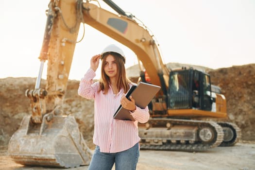 Young woman with documents in hard hat is standing on the borrow pit.