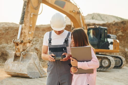 Talking about plan. Two workers is on the borrow pit at daytime together.