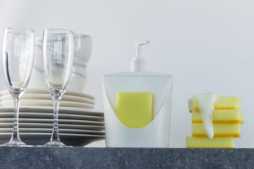 Clean dishes with dishwashing gel and yellow sponges on the kitchen table.