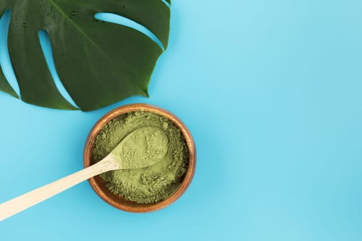 Wooden spoon with matcha tea in a wooden plate and monstera leaf on a blue background. Matcha green tea powder. copy space