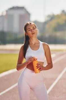 Holding bottle of watter. Young woman in sportive clothes is exercising outdoors.