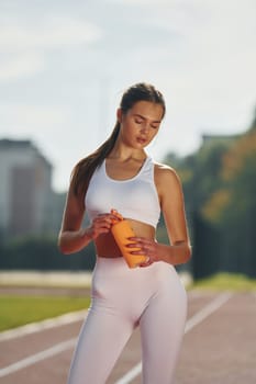 Holding bottle of watter. Young woman in sportive clothes is exercising outdoors.