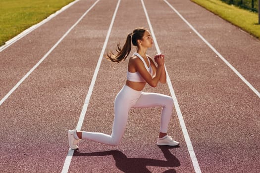 Doing squats. Young woman in sportive clothes is exercising outdoors.