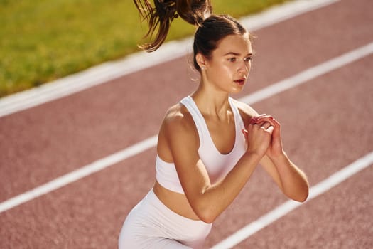 Doing squats. Young woman in sportive clothes is exercising outdoors.